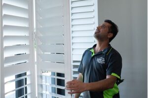 Jim's Blind Cleaning & Repairs team member fixing White Plantation Shutters on site for client